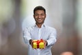 Young handsome businessman offering present box on abstract bokeh background. Royalty Free Stock Photo