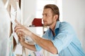 Young handsome businessman pointing finger and writing at the paper pinned to corkboard. Office background.