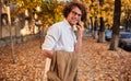 Young handsome businessman posing on the autumn street while walking outdoors and using smartphone for calling. Smiling man with Royalty Free Stock Photo