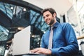 A young businessman sitting on a bench in a modern building, using laptop. Royalty Free Stock Photo