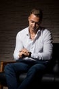 Young handsome businessman sitting with confidence on leather couch and looks to watches Royalty Free Stock Photo