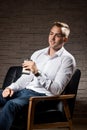 Young handsome businessman sitting on leather couch with phone in hand and thinking Royalty Free Stock Photo