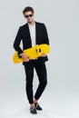 Young handsome businessman in suit and suglasses holding yellow skateboard