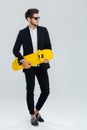 Young handsome businessman in suit and suglasses holding yellow skateboard