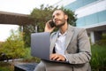 Young handsome businessman in suit using laptop and talking on cellphone outdoors Royalty Free Stock Photo
