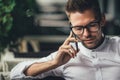 Young handsome businessman is talking on phone, sitting at table in cafe. Man in glasses makes call. Business person in Royalty Free Stock Photo