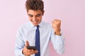 Young handsome businessman using smartphone standing over isolated pink background screaming proud and celebrating victory and Royalty Free Stock Photo