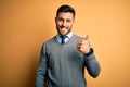 Young handsome businessman wearing elegant sweater and tie over yellow background doing happy thumbs up gesture with hand Royalty Free Stock Photo