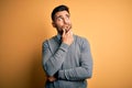 Young handsome businessman wearing elegant sweater and tie over yellow background with hand on chin thinking about question, Royalty Free Stock Photo