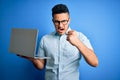 Young handsome businessman wearing glasses working using laptop over blue background annoyed and frustrated shouting with anger, Royalty Free Stock Photo