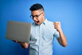 Young handsome businessman wearing glasses working using laptop over blue background screaming proud and celebrating victory and Royalty Free Stock Photo