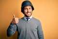 Young handsome businessman wearing military helmet over isolated yellow background doing happy thumbs up gesture with hand Royalty Free Stock Photo