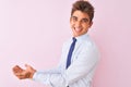 Young handsome businessman wearing shirt and tie standing over isolated pink background pointing aside with hands open palms Royalty Free Stock Photo