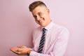 Young handsome businessman wearing shirt and tie standing over isolated pink background pointing aside with hands open palms Royalty Free Stock Photo