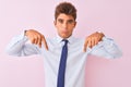 Young handsome businessman wearing shirt and tie standing over isolated pink background Pointing down looking sad and upset, Royalty Free Stock Photo