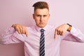 Young handsome businessman wearing shirt and tie standing over isolated pink background Pointing down looking sad and upset, Royalty Free Stock Photo