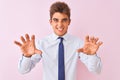 Young handsome businessman wearing shirt and tie standing over isolated pink background smiling funny doing claw gesture as cat,