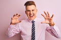 Young handsome businessman wearing shirt and tie standing over isolated pink background smiling funny doing claw gesture as cat,