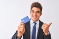 Young handsome businessman wearing suit holding credit card over isolated white background pointing and showing with thumb up to Royalty Free Stock Photo