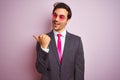 Young handsome businessman wearing suit and sunglasses over isolated pink background smiling with happy face looking and pointing Royalty Free Stock Photo