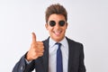 Young handsome businessman wearing suit and sunglasses over isolated white background doing happy thumbs up gesture with hand Royalty Free Stock Photo