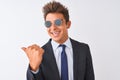 Young handsome businessman wearing suit and sunglasses over isolated white background smiling with happy face looking and pointing Royalty Free Stock Photo