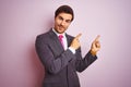 Young handsome businessman wearing suit and tie standing over isolated pink background smiling and looking at the camera pointing Royalty Free Stock Photo