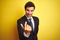 Young handsome businessman wearing suit and tie standing over isolated yellow background Beckoning come here gesture with hand