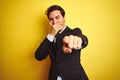 Young handsome businessman wearing suit and tie standing over isolated yellow background laughing at you, pointing finger to the Royalty Free Stock Photo