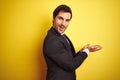 Young handsome businessman wearing suit and tie standing over isolated yellow background pointing aside with hands open palms Royalty Free Stock Photo