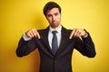 Young handsome businessman wearing suit and tie standing over isolated yellow background Pointing down looking sad and upset, Royalty Free Stock Photo