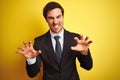 Young handsome businessman wearing suit and tie standing over isolated yellow background smiling funny doing claw gesture as cat,