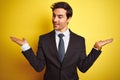 Young handsome businessman wearing suit and tie standing over isolated yellow background smiling showing both hands open palms, Royalty Free Stock Photo