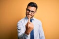 Young handsome businessman wearing tie and glasses standing over yellow background Beckoning come here gesture with hand inviting