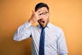 Young handsome businessman wearing tie and glasses standing over yellow background peeking in shock covering face and eyes with Royalty Free Stock Photo