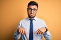 Young handsome businessman wearing tie and glasses standing over yellow background Pointing down looking sad and upset, indicating Royalty Free Stock Photo