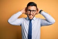 Young handsome businessman wearing tie and glasses standing over yellow background relaxing and stretching, arms and hands behind Royalty Free Stock Photo