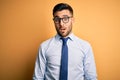 Young handsome businessman wearing tie and glasses standing over yellow background In shock face, looking skeptical and sarcastic,