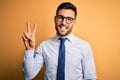 Young handsome businessman wearing tie and glasses standing over yellow background showing and pointing up with fingers number two Royalty Free Stock Photo