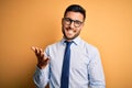 Young handsome businessman wearing tie and glasses standing over yellow background smiling cheerful with open arms as friendly Royalty Free Stock Photo