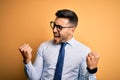 Young handsome businessman wearing tie and glasses standing over yellow background very happy and excited doing winner gesture Royalty Free Stock Photo