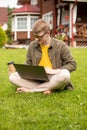 Young handsome businessman works on laptop outdoors, sits with coffee on grass