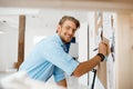 Young handsome businessman writing on the paper pinned to corkboard, looking in camera smiling. Office background.