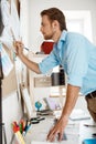 Young handsome businessman writing at the paper pinned to corkboard. Office background.