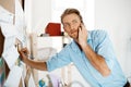 Young handsome businessman writing at the paper pinned to corkboard, talking on phone. Office background.