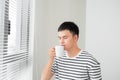 Young handsome carefree man near modern full length window enjoying a cup of coffee while looking outside, good morning Royalty Free Stock Photo