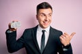 Young handsome caucasian business man holding finance credit card over pink background pointing and showing with thumb up to the Royalty Free Stock Photo