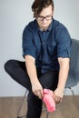 Young handsome caucasian male with dark curly hair pulls on bright pink sock with piglet.