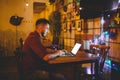 A young handsome Caucasian man with beard and toothy smile in a red checkered shirt is working behind a gray laptop sitting at a w Royalty Free Stock Photo