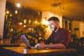 A young handsome Caucasian man with beard and toothy smile in a red checkered shirt is working behind a gray laptop sitting at a w Royalty Free Stock Photo